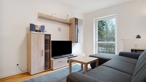 A living room with a TV, sofa, and a window with a view of trees. - Apartment 'Meer-Natur-Idyll' with Wi-Fi (Peenemünde)