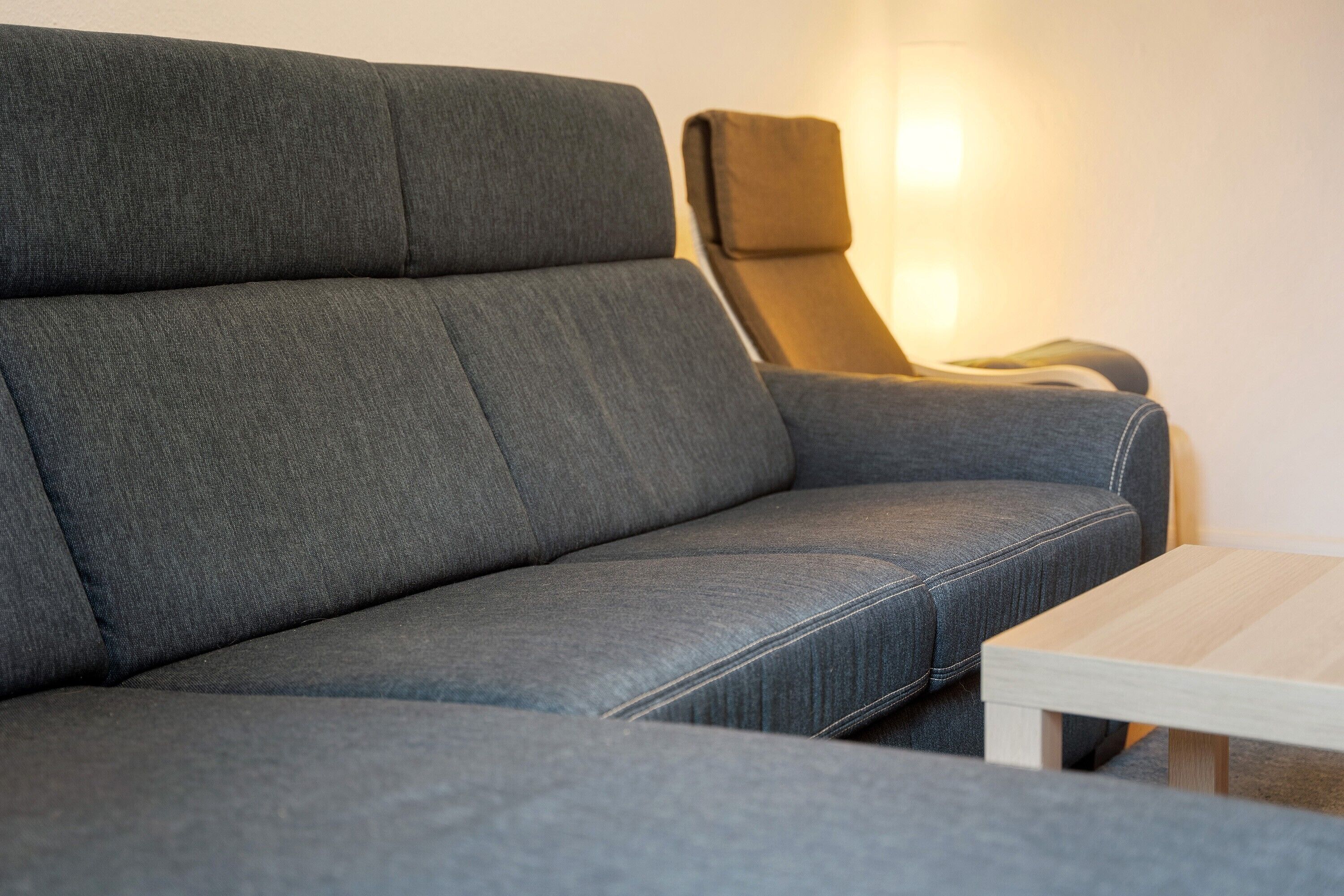 A grey sofa with a wooden coffee table in a room with a light source on the wall.