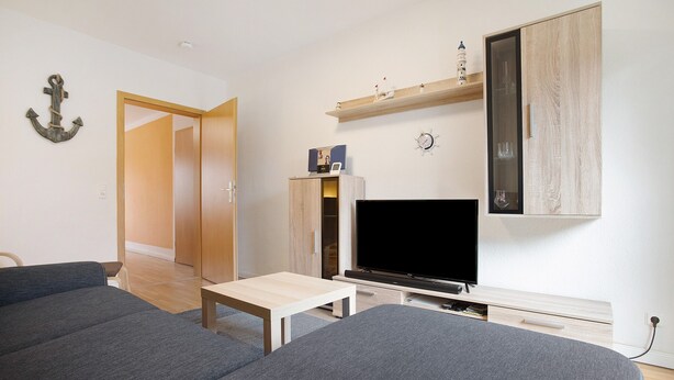 A modern living room with a flat-screen TV, a sofa, a coffee table, and a wooden cabinet with shelves. - Apartment 'Meer-Natur-Idyll' with Wi-Fi (Peenemünde)