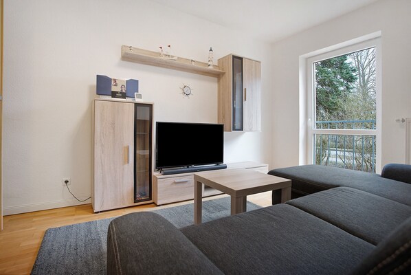 A modern living room with a flat-screen TV, a sofa, a small table, and a cabinet.