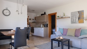 A modern living space with a dining area, kitchen, and a sofa with colorful cushions. - Cozy Log Cabin in the Harz with Private Terrace & Garden (Bad Sachsa)