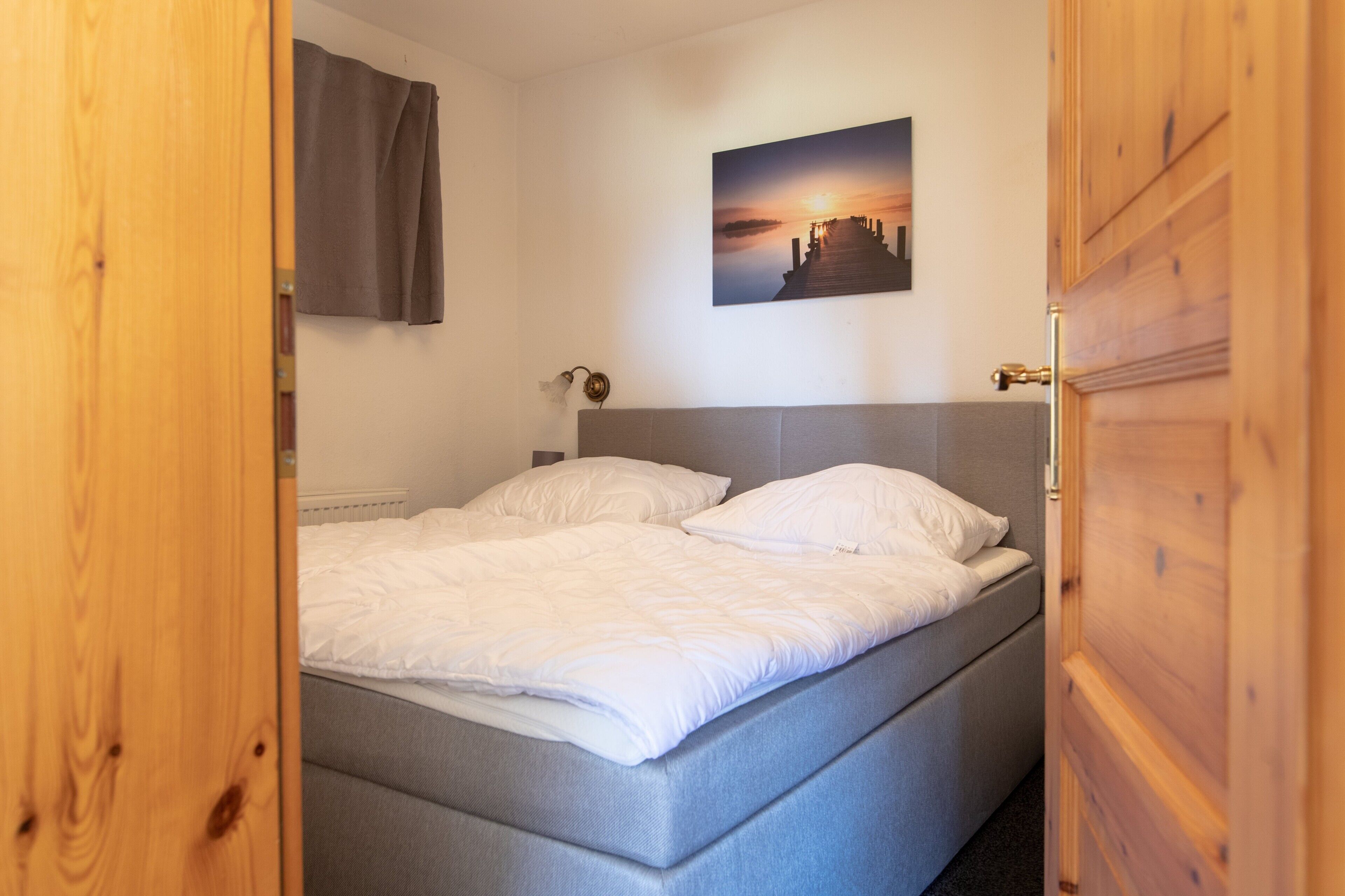 A bedroom with a bed, a headboard, a wall-mounted picture, and a wooden door.