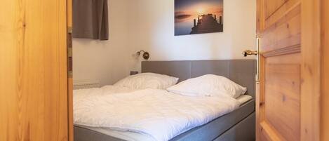 A bedroom with a bed, a headboard, a wall-mounted picture, and a wooden door.