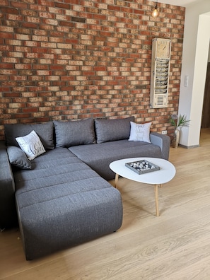 Un sofá modular con almohadones, una mesa de centro blanca y una pared de ladrillo con un reloj.