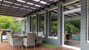 A covered patio with a dining table and chairs, a grill, and a view of a swimming pool. - Holiday Home 'Beautiful View' in the Harz with Mountain View, Private Terrace and Wi-Fi (Walkenried)