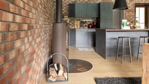 A modern kitchen with brick walls, a wood-burning stove, and a bar area with stools. - Holiday Home 'Beautiful View' in the Harz with Mountain View, Private Terrace and Wi-Fi (Walkenried)