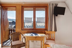 Une pièce avec une table en bois, une chaise en osier et une vue dégagée sur l’extérieur grâce à une grande fenêtre.