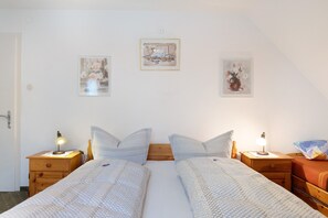 Ein Schlafzimmer mit zwei Betten, Holznachttischen, Nachttischlampen und Wandbildern.