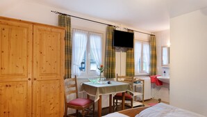 A bedroom with a bed, a table with chairs, a TV, and a window with curtains. - Room '4 with WC and Shower' with Shared Terrace and Wi-Fi (Lenzkirch)