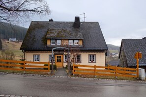 Ein zweistöckiges Haus mit geneigtem Dach, Holzzaun und gepflasterter Auffahrt.