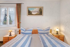 Ein Schlafzimmer mit einem Bett, zwei Nachttischen, einem Fenster mit Vorhängen und einem Bild an der Wand.