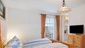 A bedroom with a bed, a television, a wooden dresser, and a window with curtains. - Room 'Doppelzimmer 1' with Shared Terrace, Balcony and Wi-Fi (Lenzkirch)