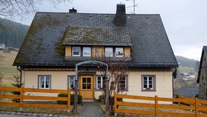 A two-story building with a sloped roof, a wooden front gate, and a paved entrance. - Room 'Doppelzimmer 1' with Shared Terrace, Balcony and Wi-Fi (Lenzkirch)