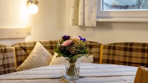 Una habitación con una mesa, un jarrón con flores, un sofá y una ventana con cortinas.