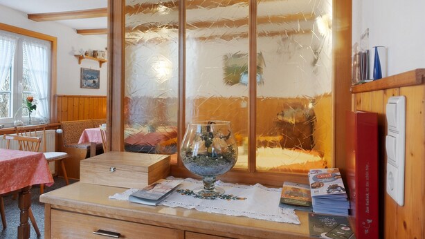 Una habitación con una mesa de madera, un aparador de cristal con vistas y un libro rojo a la derecha.