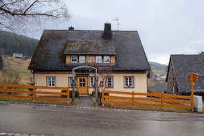 Ein zweistöckiges Haus mit geneigtem Dach, Holzzaun und gepflasterter Auffahrt.