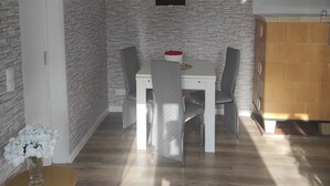 Comedor con una mesa blanca y sillas grises, una lámpara colgante negra y un armario de madera.