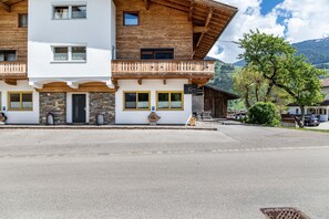 Ein zweistöckiges Gebäude mit Holzbalkon, Steinfassade und Blick auf die Berge.