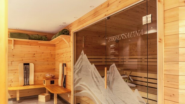 Un sauna en bois, doté de bancs et d’une porte en verre sur laquelle on peut lire le nom « ZIRBENSAUNA ».
