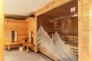 Una sauna de madera con bancos y una puerta de cristal, con el nombre 'ZIRBENSAUNA' a la vista.