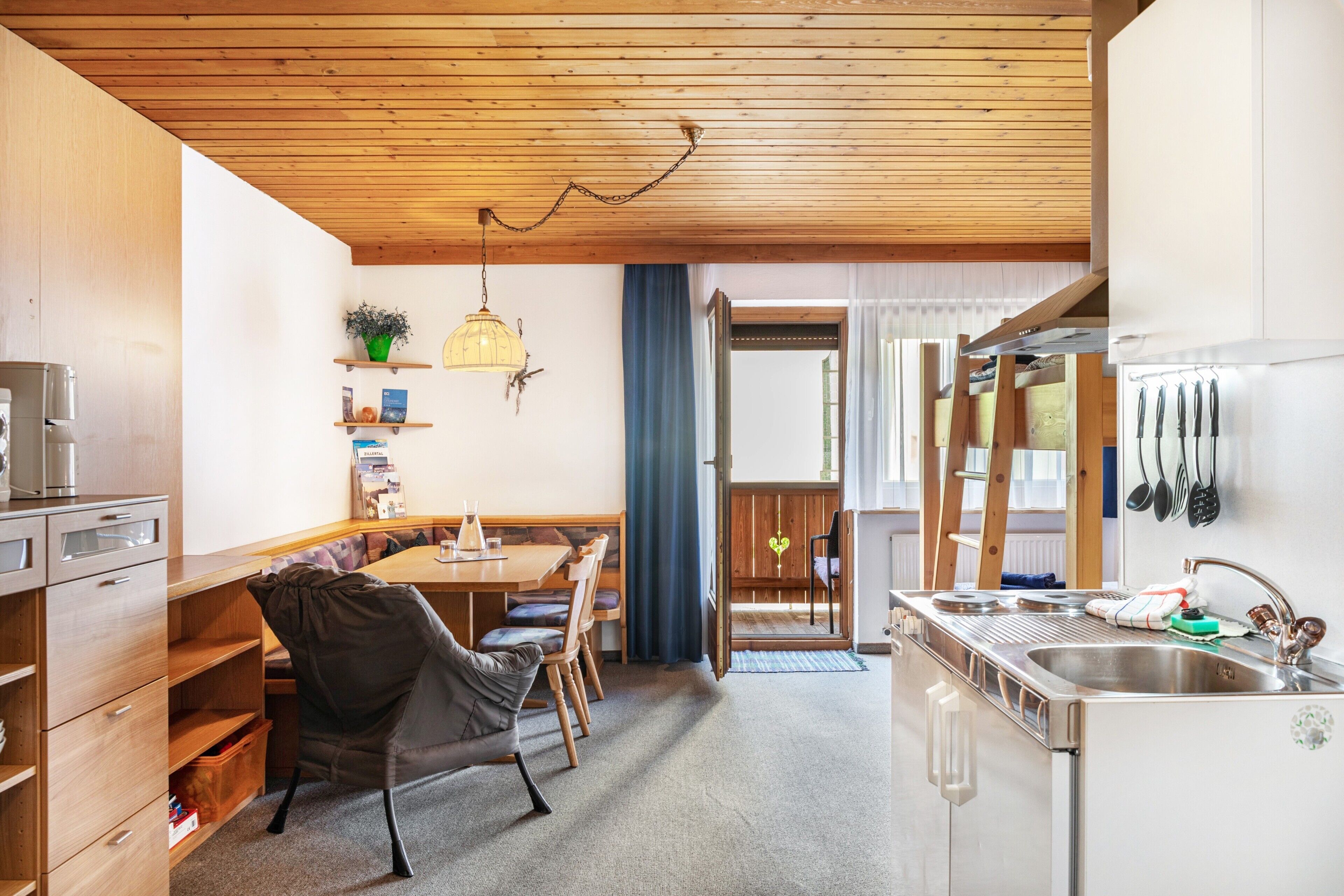 Cocina compacta con armarios de madera, comedor con banco y vistas al exterior.