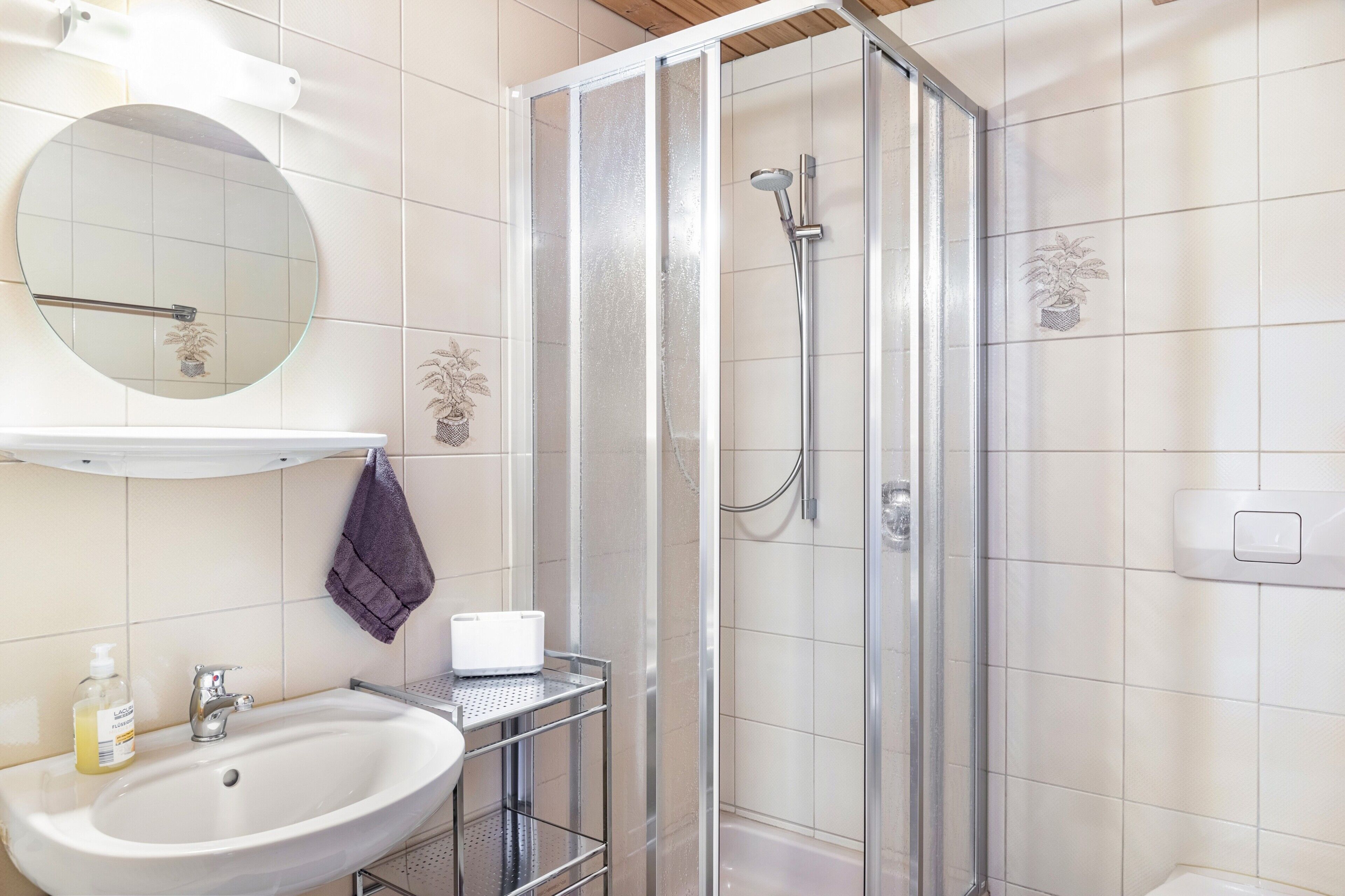 A bathroom with a sink, mirror, shower, and towel rack.