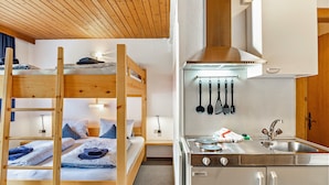 Un lit superposé avec une tête de lit en bois, une cuisine dotée d’un évier en acier inoxydable et d’ustensiles de cuisine suspendus.