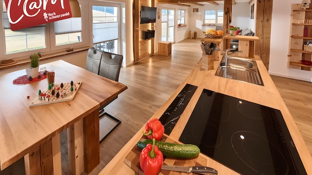 A modern kitchen with a wooden table, a cutting board with vegetables, a knife, and a built-in stove. - Holiday Home Wendelhof Apartment Fuchsbau (Eisenbach (Hochschwarzwald))