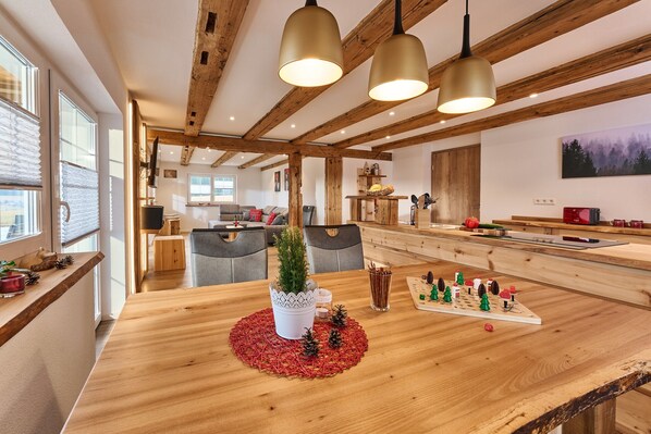 A spacious kitchen with wooden beams, a dining table with a red placemat, and a small Christmas tree.