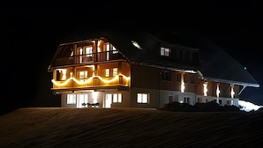 A large, multi-story building with a sloped roof, illuminated windows, and a balcony with string lights. - Holiday Home Wendelhof Apartment Fuchsbau (Eisenbach (Hochschwarzwald))