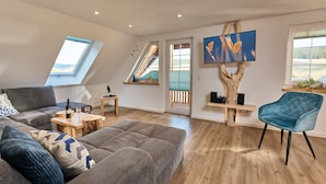 Un salon moderne avec un canapé, un fauteuil bleu, une table basse en bois et un téléviseur fixé sur le tronc d’un arbre.