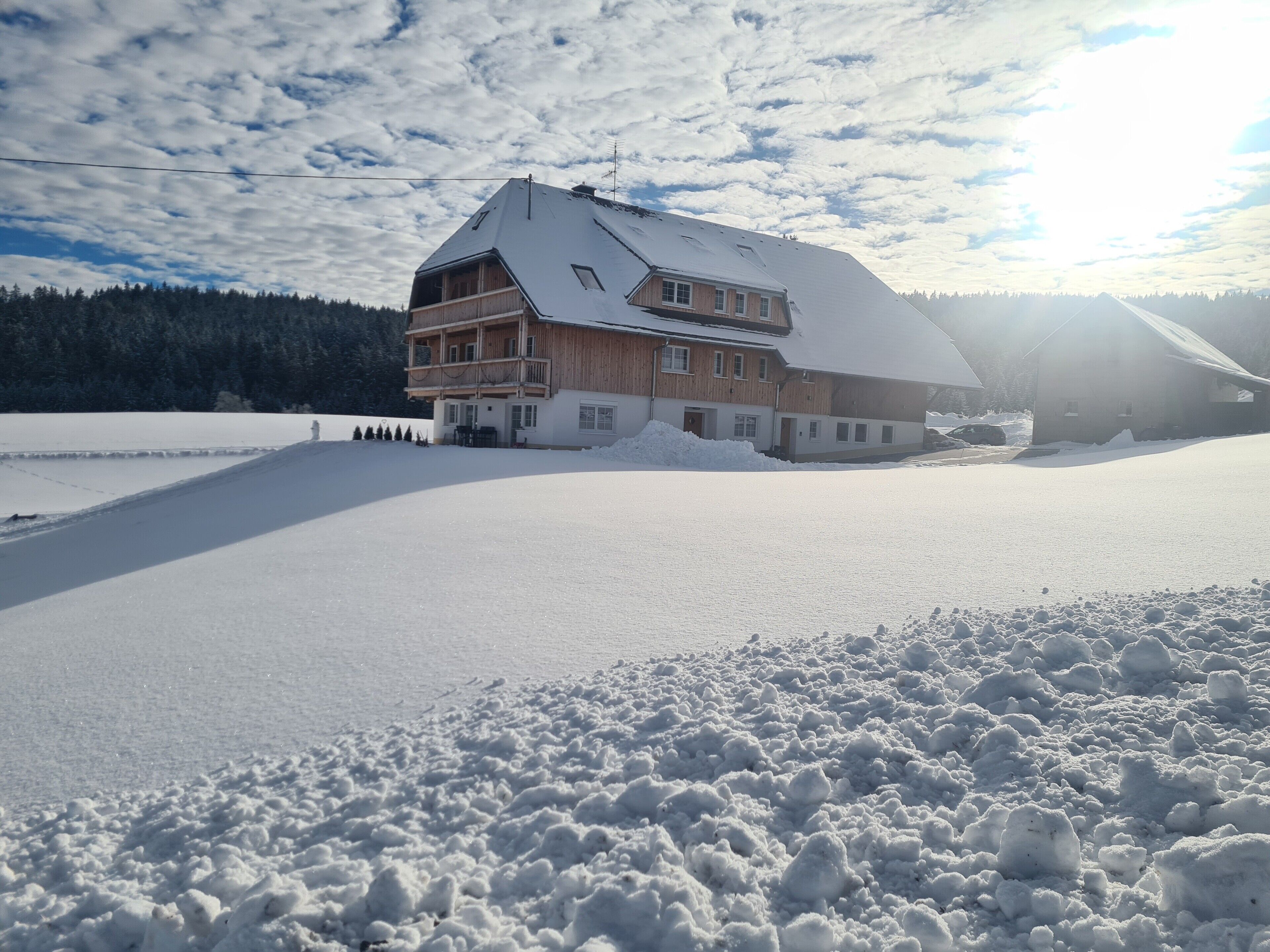 Ein großes, mehrstöckiges Holzhaus mit geneigtem Dach, umgeben von verschneitem Gelände und einem bewaldeten Hintergrund.