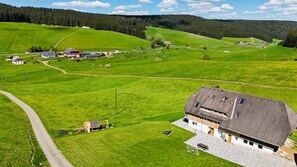 Paisaje rural con una casa de techo inclinado, un camino pavimentado y una pequeña zona de estar al aire libre.