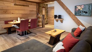 Une pièce chaleureuse avec un plafond en bois, un coin repas avec une table et des chaises, un canapé avec des coussins rouges et une étagère murale avec des haut-parleurs.