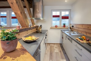 Une cuisine moderne avec des poutres en bois, un grand îlot central et une vue sur un paysage enneigé par les fenêtres.