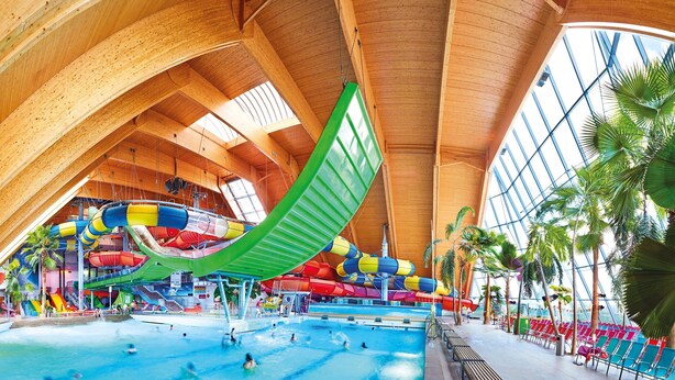 Un parc aquatique intérieur doté d’un grand toboggan, de plusieurs piscines et d’un haut plafond en bois.