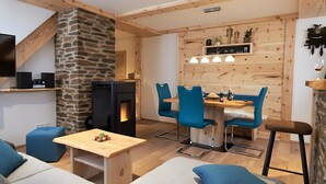 Ein gemütlicher Wohnbereich mit Steinwand, Holzboden und einem Essbereich mit blauen Stühlen und einem Holztisch.