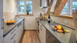 Eine moderne Küche mit einem großen Fenster, Holzbalken und einer Auswahl an Küchenutensilien sowie frischem Obst und Gemüse auf der Arbeitsfläche.