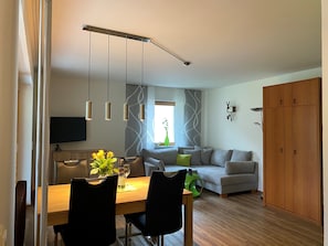 A modern living room with a sofa, dining table, chairs, and a TV.