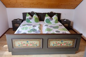 Une chambre à coucher avec une tête de lit en bois, deux tables de chevet, un lit avec une literie à motifs et des panneaux décoratifs à motifs floraux sur le cadre du lit.