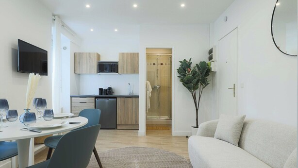 A modern living room with a sofa, a dining table with chairs, a kitchen area with cabinets and a microwave, and a glass shower door. - Flat 1BDR/2P Roland Garros/Parc des (Boulogne-Billancourt)