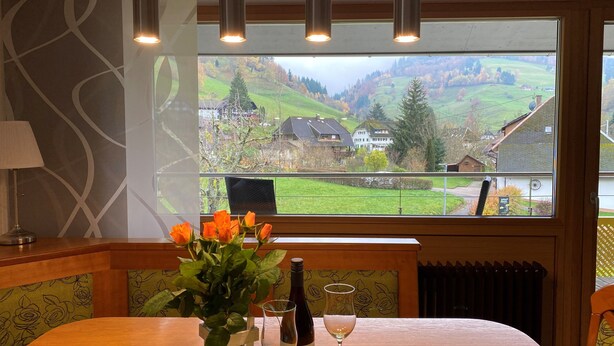 A dining table with a bottle of wine, a glass, and a vase of flowers.