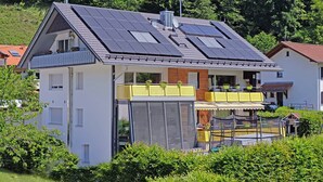 A modern house with solar panels, a balcony with potted plants, and a covered outdoor seating area.
