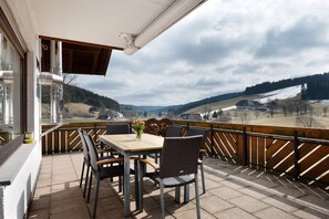 Un balcon avec une table et des chaises, donnant sur un paysage vallonné.