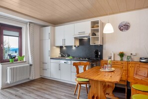 A modern kitchen with white cabinets, a wooden dining table, and a view through the window.