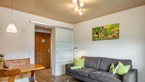 Ein Zimmer mit einem Holzespeisetisch, einem grauen Sofa mit Kissen, einem Schmetterlingsbild und einer Holztür.