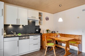 A modern kitchen with white cabinets, a black countertop, and a wooden dining table with green chairs.