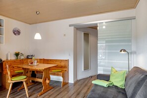 A dining area with a wooden table and benches, a sofa with cushions, a lamp, and a window with a view.