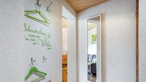Ein Flur mit einer weißen Wand mit Struktur, einem grünen Kleiderbügel und einem Spiegel, der einen Raum mit einem grauen Sofa reflektiert.