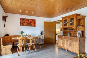 Una mesa de comedor de madera con sillas, un banco de madera, un aparador con puertas de cristal y un cuadro en la pared.